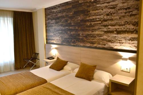 a hotel room with two beds and a brick wall at Hotel Alda San Carlos in Santiago de Compostela