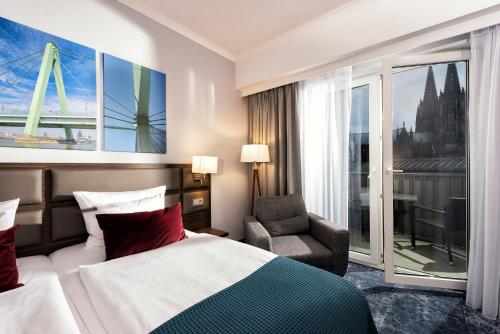a hotel room with a bed and a chair and a window at Wyndham Köln in Cologne