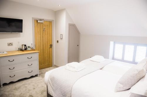 a bedroom with two beds and a dresser with a television at Rutland Water Courtyard Rooms in Oakham