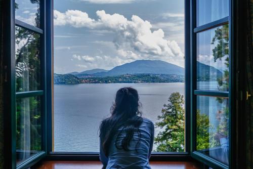 a woman sitting in front of a window looking out at the water at Relais Casali della Cisterna in Belgirate