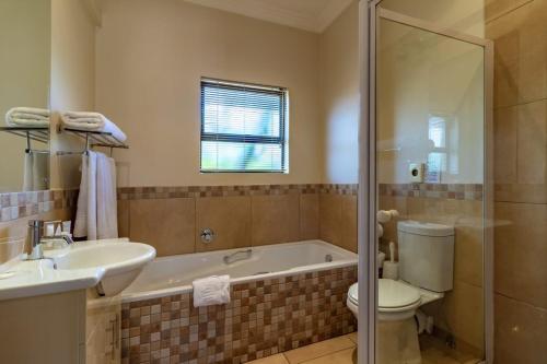 a bathroom with a tub and a toilet and a sink at Hoyohoyo Chartwell Lodge in Johannesburg