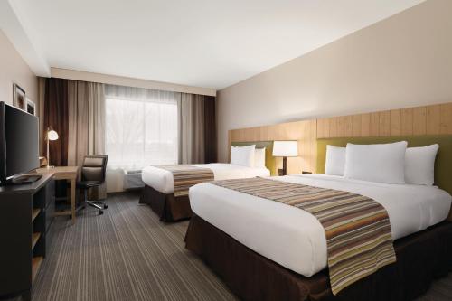 a hotel room with two beds and a desk and a television at Country Inn & Suites by Radisson, Belleville, ON in Belleville