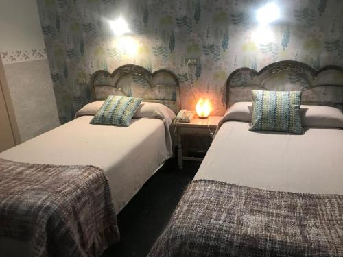 a room with two beds and a table with a lamp at Hostal Pirineos in Barbastro
