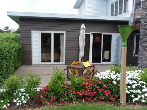 a patio with an umbrella and flowers in front of a house at The Orchard in Whakamarama