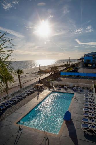 a swimming pool next to a beach with chairs and the sun at South Beach Biloxi Hotel & Suites in Biloxi