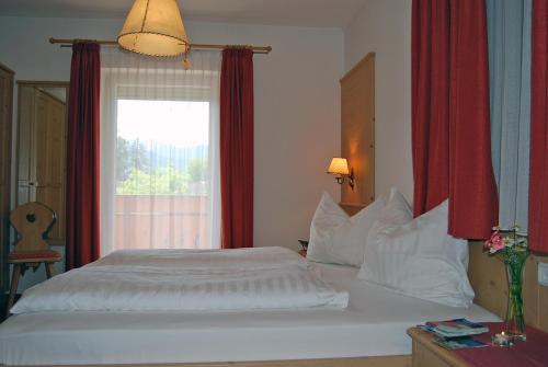 a bedroom with a white bed with red curtains and a window at Gasthof Weidmannshof in Bressanone