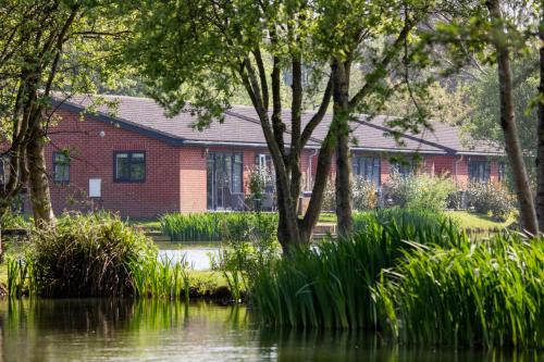 a red brick house next to a body of water at The Lakes Rookley in Rookley