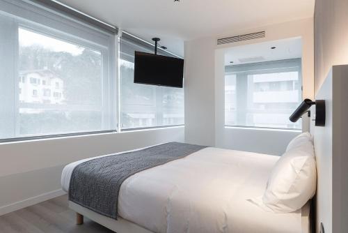 a white bedroom with a bed and a large window at Hotel Distrito Oeste in Donostia-San Sebastián