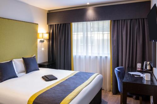 a hotel room with a bed and a desk and a window at Mercure Newbury West Grange Hotel in Thatcham
