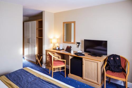 a hotel room with a desk with a television and chairs at Mercure Newbury West Grange Hotel in Thatcham