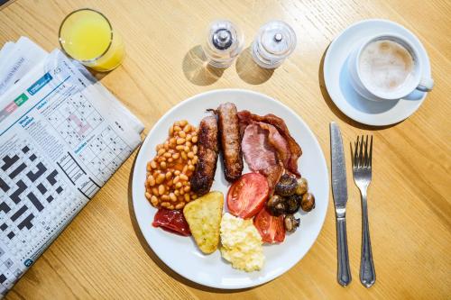 a plate of breakfast food on a table with a newspaper at Mercure Newbury West Grange Hotel in Thatcham
