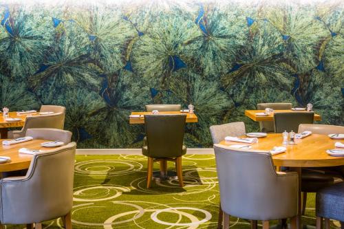 a dining room with tables and chairs and a wall of palm trees at Mercure Newbury West Grange Hotel in Thatcham