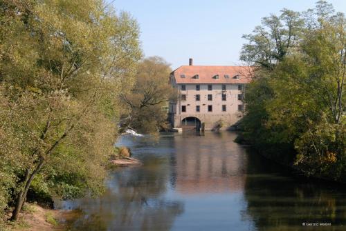 a river in front of a building with a bridge at Auberge Saint Walfrid Hôtel Restaurant & Spa in Sarreguemines