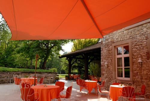 a patio with tables and chairs under an orange umbrella at Auberge Saint Walfrid Hôtel Restaurant & Spa in Sarreguemines