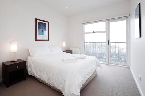 a white bedroom with a large bed and a window at Apartment K2 14 in Mount Buller