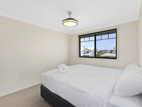 a white bedroom with a bed and a window at North Entrance Beach House in The Entrance