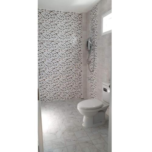a bathroom with a toilet and a tiled wall at Khaohom House in Chiang Mai