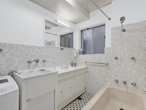ein weißes Badezimmer mit einer Badewanne, einem Waschbecken und einem Spiegel in der Unterkunft Dolphin Court 5 in The Entrance