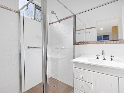 a white bathroom with a shower and a sink at Lake Edge Cottage in Budgewoi