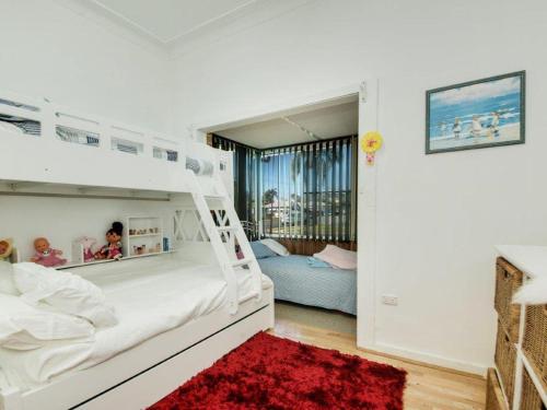 a white bedroom with a bunk bed and a red rug at Manning Pool House in The Entrance