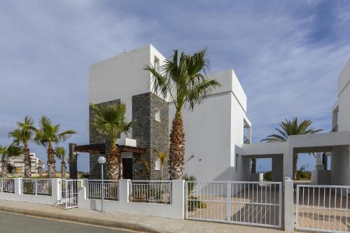 a white building with palm trees in front of it at Faros BeachFront Villa in Pervolia