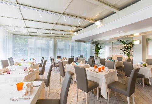 un restaurante con mesas y sillas blancas y ventanas en Hotel Luxor, en Milano Marittima