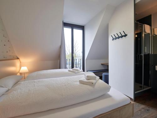 a white bedroom with two beds and a large window at Radhotel am Gleis in Radolfzell am Bodensee