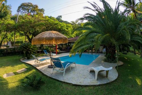 a pool in a yard with chairs and a umbrella at Pousada Pedras Brancas in Niterói