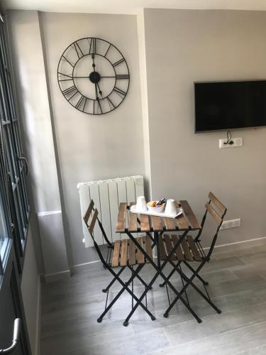 une table, deux chaises et une horloge sur un mur dans l'établissement La bonbonnière de Sofi, à Honfleur