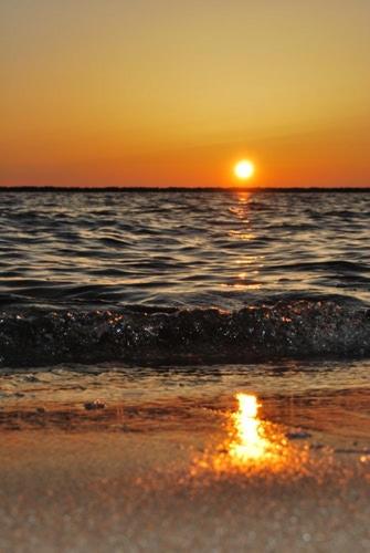 a sunset on the beach with the sun setting over the ocean at Villa Bougenvilia Tomas in Tučepi