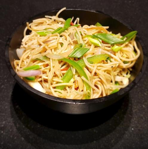 a black bowl filled with noodles and green onions at Hotel Stellar in Vadodara