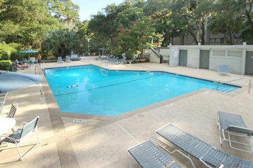 a large blue swimming pool with chairs and trees at Ocean Breeze 23 in Hilton Head Island