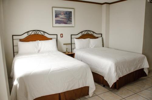 two beds in a hotel room with white sheets at Hotel Gardenia Inn in San Salvador