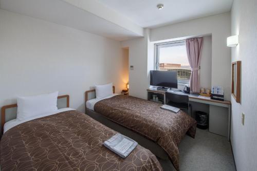 a hotel room with two beds and a desk with a computer at Hotel Airport Komatsu in Komatsu