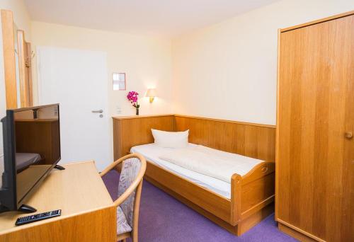 Kleines Zimmer mit einem Bett, einem Schreibtisch und einem TV. in der Unterkunft Hotel Müritzlicht in Waren (Müritz)