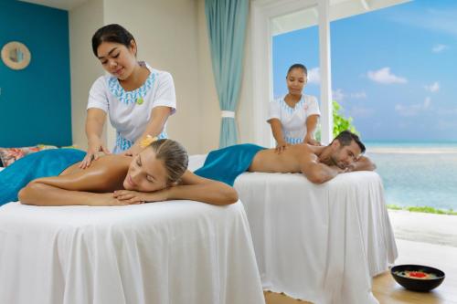 a woman giving a man a massage on two beds at Kandima Maldives in Kudahuvadhoo