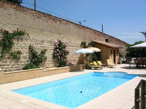 a swimming pool in front of a brick wall with an umbrella at Les Jardins de l'Hacienda in Tarare