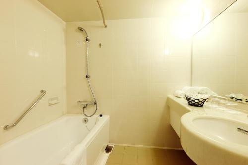 ein weißes Badezimmer mit einem Waschbecken, einer Badewanne und einer Dusche in der Unterkunft Hotel Konigs-Krone Kobe in Kōbe