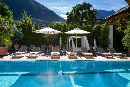 a woman standing next to a swimming pool with chairs and umbrellas at Hotel Löwenhof in Bressanone