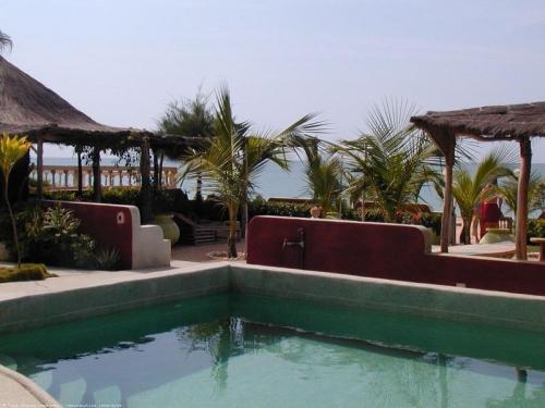 uma piscina em frente a um resort com palmeiras em A Keurmaya em Saly Portudal