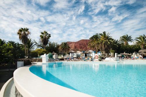a swimming pool at a resort with palm trees at Sandos Atlantic Gardens in Playa Blanca