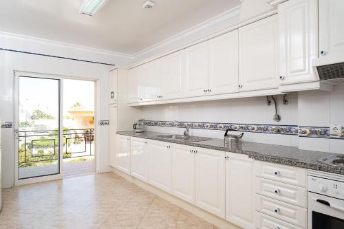a kitchen with white cabinets and a large window at Apartamentos Benvindo in Albufeira