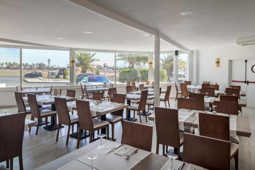 un restaurante con mesas, sillas y ventanas en Sandos Atlantic Gardens, en Playa Blanca
