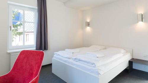 a white bed with a red chair and a window at Pivovar Falkenštejn in Krásná Lípa
