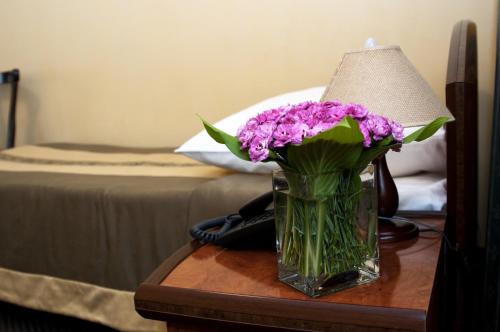 a vase of purple flowers on a table with a lamp at Wien Hotel in Lviv