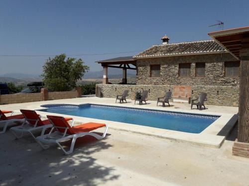 a swimming pool with chairs and a house at Casa rural Los Caballos Finca Los Pelaeros in Alora