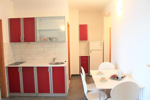 a kitchen with red cabinets and a table and a sink at Apartmani Marija in Duće