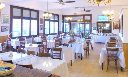 una sala da pranzo con tavoli e sedie bianchi e finestre di Hotel Imperio a Mar del Plata