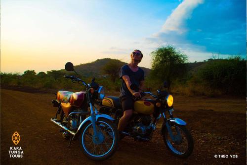 a man sitting on a motorcycle on the road at Kara-Tunga Safari Camp in Moroto
