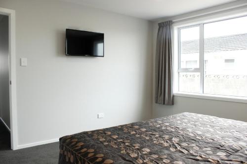 a bedroom with a bed and a tv and a window at Colonial Motel in Invercargill